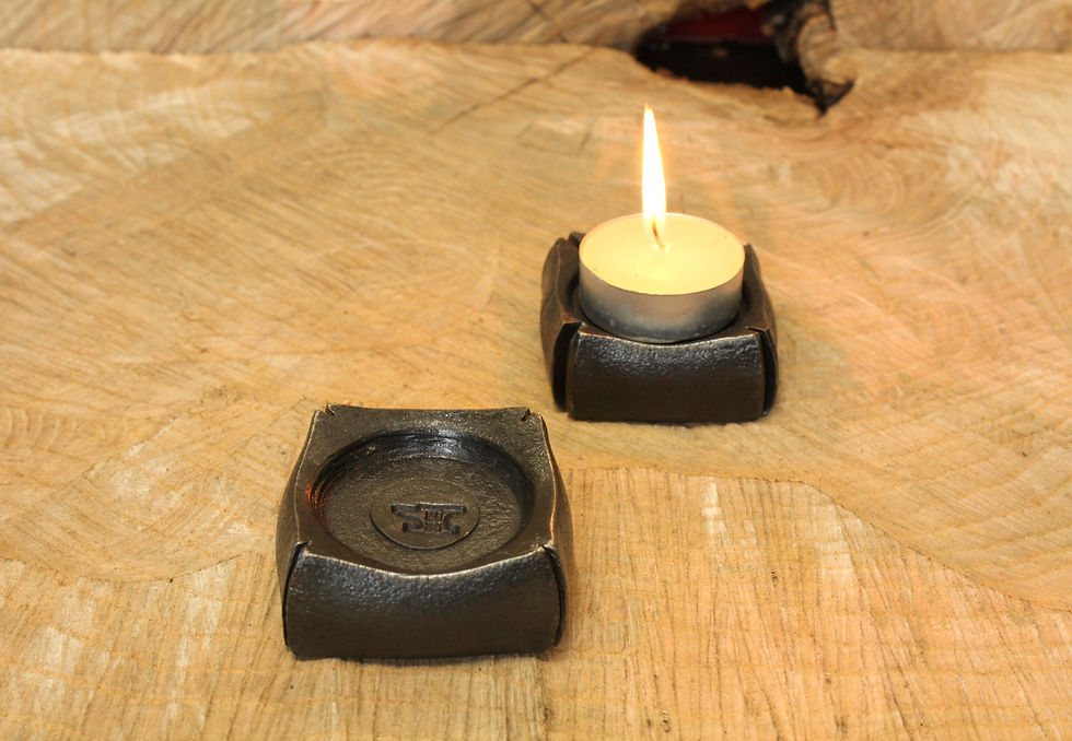 Two hand-forged iron tealight holders on wood; one lit, one empty with stamped logo.