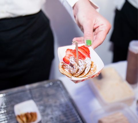 Hand presenting a serving of Oma’s Poffertjes topped with strawberries and powdered sugar.