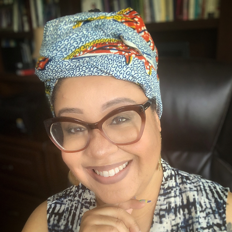 Dr. Tiffany D. Pogue (Educator and Cultural Worker) smiles at the camera in front of a bookshelf.