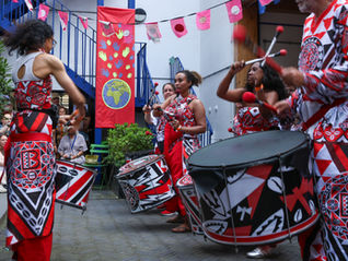 Batala London drummer playing a large Fundo bass drum with other drummers behind.