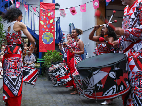 Batala London drummer playing a large Fundo bass drum with other drummers behind.