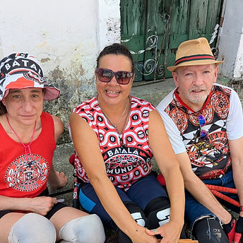 Three Batala members in a group photo, sat on the site of a street in Salvador, Brazil. 