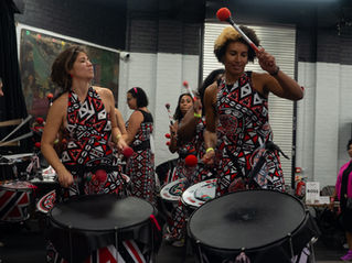 Batala London drummers performing samba-reggae at Samba de Bamba UK, with raised beaters, colourful costumes and an audience watching at Maxilla Social Club.