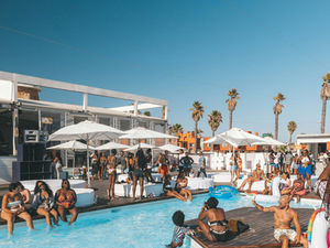 summer day in a beach bar with a pool, people enjoying sun, white umbrellas and palms in the background