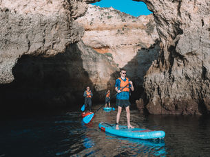 three men on stand up paddles on the ocean surrounded by cliffs