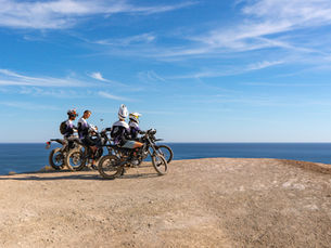 four riders on surrons in motocross clothes standing on the cliff with the sea and blue sky in the background