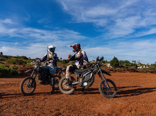 two people in motocross clothes sitting on surron dirtbikes and talking