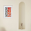 Miniatura: a mockup of a watercolour painting of red and black strikes and symbols hanging in a bright room with an arch shelf and vase