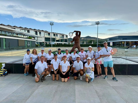 Tennis players in white shirts pose by a statue at a club