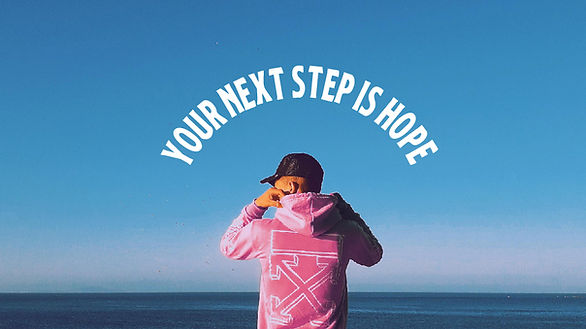 A man in a pink hoodie and black hat looking over the water with a caption that says "Your Next Step is Hope"