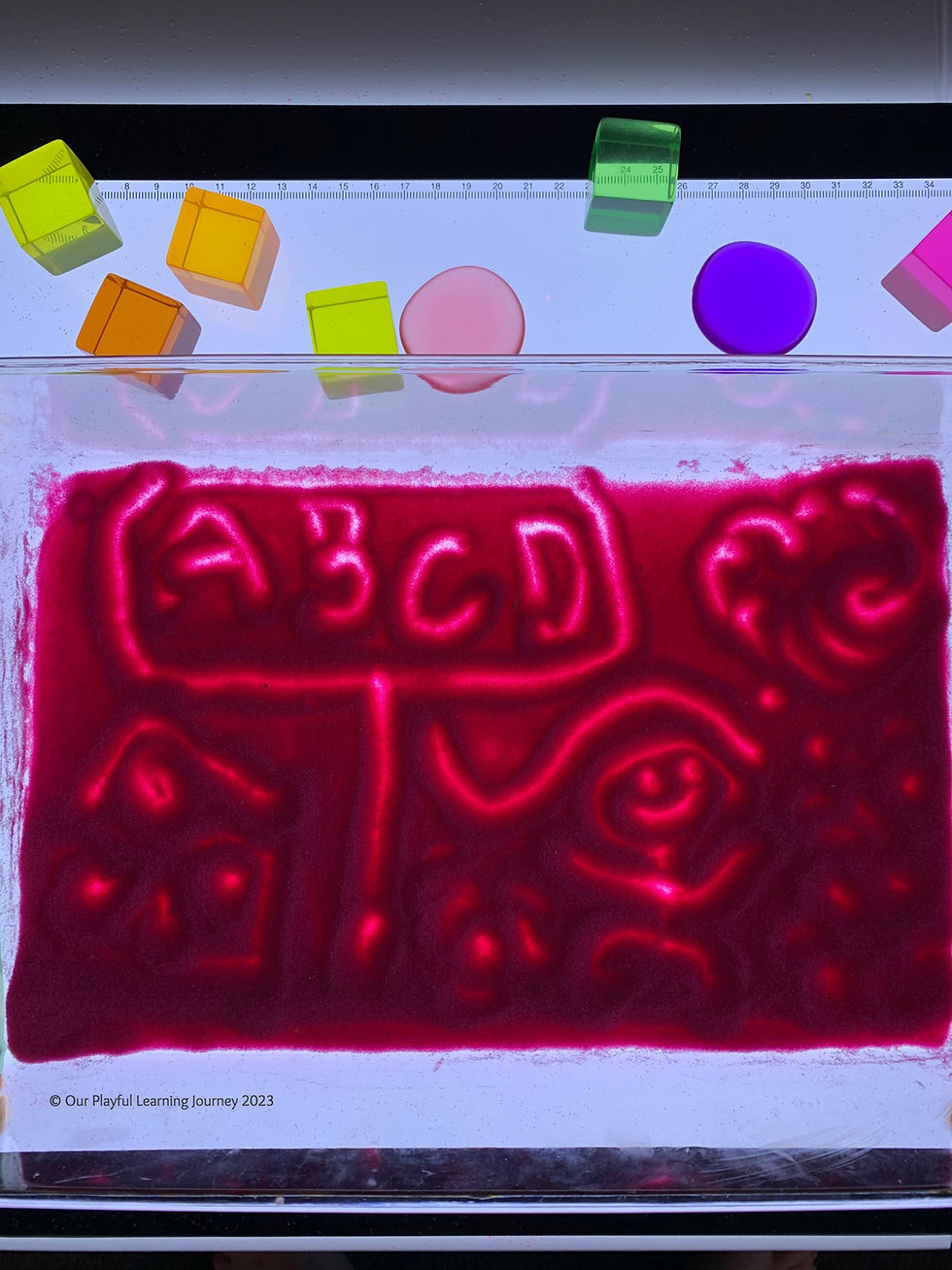 Light panel play idea for kids using a sand tray for drawing and writing.