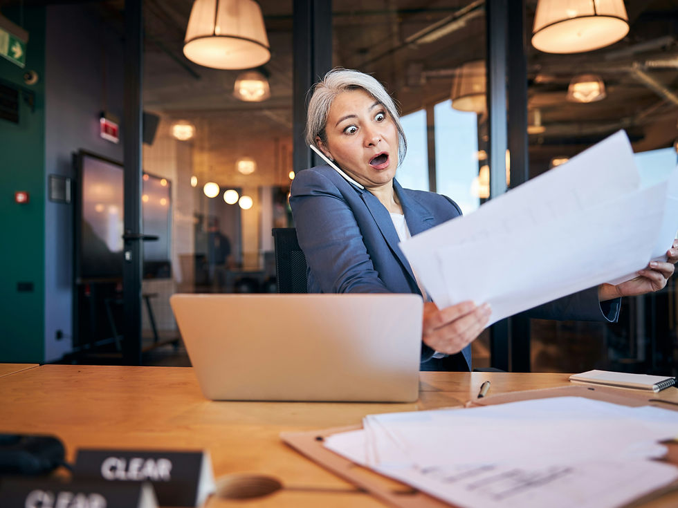 Woman in an office, surprised while holding papers, talking on phone. Laptop on desk, modern interior with hanging lamps, clear sign.