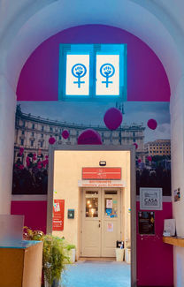 Ingresso del ristorante/caffetteria "L'una e l'altra", preceduto da un arco con la gigantografia di una manifestazione femminista a Piazza della Repubblica (Roma) sormontata a sua volta dal simbolo della lotta femminista.