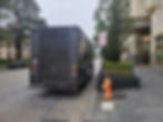 A delivery truck is parked in a restricted area next to a fire hydrant and a sign that reads 'No stopping any time.' The location appears to be in front of a commercial building with decorative planters. The truck is partially blocking the sidewalk and fire hydrant, indicating a common parking violation.