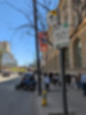A busy Toronto sidewalk featuring a cluster of curbside signs, including one designating a taxi stand within 3 meters of a hydrant, and another for pay parking enforced between 8 AM and 9 PM. A yellow fire hydrant with a blue top is visible at the curb. Nearby are parked motorcycles, pedestrians, and a line of people outside a historic building. CN Tower banners and city buildings are seen in the background.