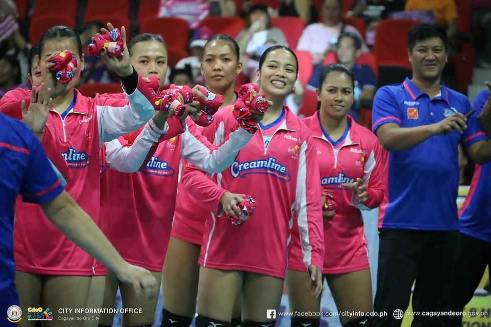 Pink Creamline volleyball players and staff smile and wave red towels in an indoor arena; Cagayan de Oro City info text below.