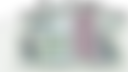 Two people working with charts and checklists on a computer screen. One writes on a clipboard, the other types on a laptop.