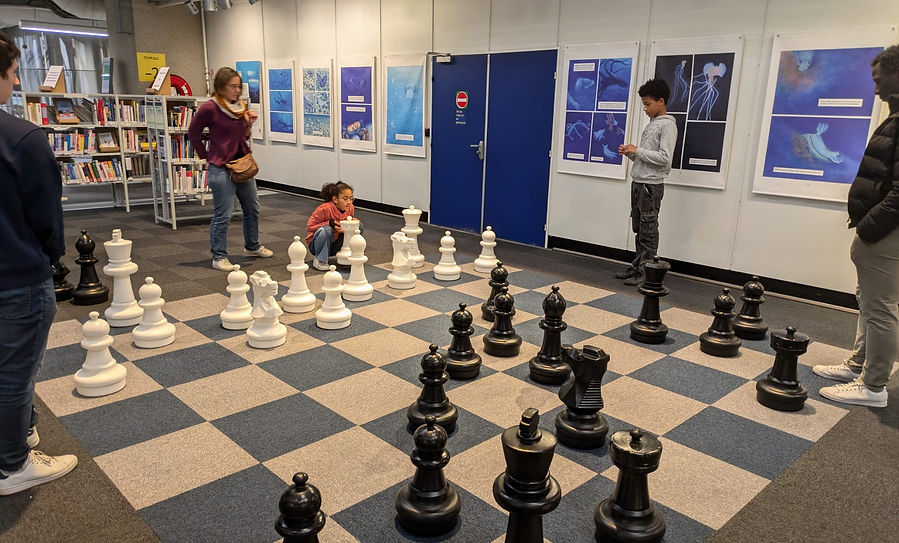 ChessMates workshop at the Cité des sciences: children and teenagers playing on a giant chessboard in a library.