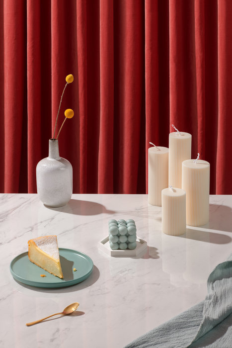 Lifestyle-Fotografie für einen Onlineshop: Keramikteller mit Kuchen, Vase und Kerzen auf weißem Marmortisch.