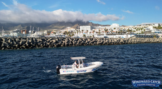 Fotografía tomada desde un dron de la embarcación Windward Catch Fishing Charter navegando en el mar azul frente a la escollera del puerto de Tenerife.