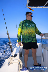Hombre con gafas de sol y ropa de pesca de pie en la cubierta delantera de un barco a pleno sol.