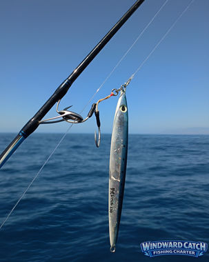 Primer plano desde nuestro barco Windward Catch Fishing Charter; un señuelo artificial alargado azul y plata con anzuelo asistente enganchado a la anilla de una caña, con el mar abierto en movimiento de fondo en el Sur de Tenerife.