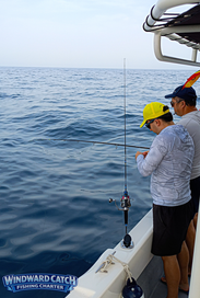 Dos clientes pescando concentrados desde la borda del barco Windward Catch, uno de ellos con gorra amarilla, durante un chárter compartido en Tenerife