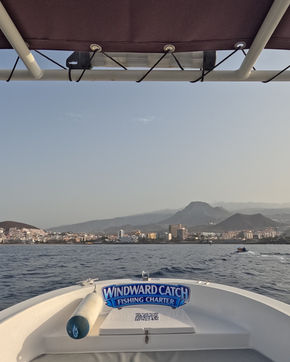 Vista frontal desde la proa acolchada del barco Windward Catch Fishing Charter regresando hacia la costa de la isla bajo la luz del sol.