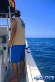 Hombre con camiseta amarilla sin mangas mirando hacia el horizonte desde la borda del barco en un día despejado.