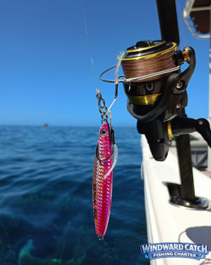 Primer plano de un jig alargado de color rosa con anzuelo asistido (assist hook) montado junto a un carrete de spinning en Windward Catch Fishing Charter.
