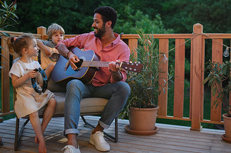Young African american man enjoys playing the guitar with little children accompaining him with instruments on patio in garden in summer.