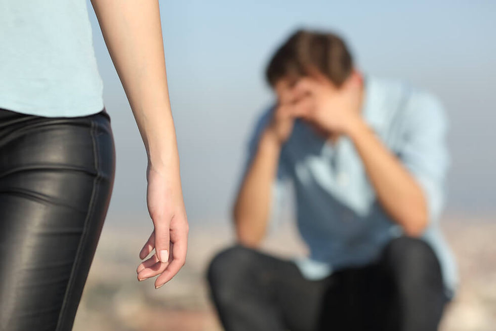 A woman walks away in foreground, while a man sits blurred in background with head in hands. Clear sky evokes a somber mood.