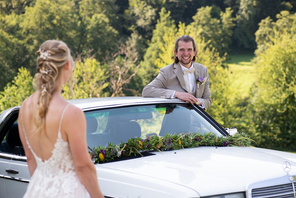 Hochzeitsfotograf Heppenheim – Bräutigam lacht die Braut an über geschmücktem Hochzeitsauto, echtes Duchenne-Lächeln mit Augenfalten