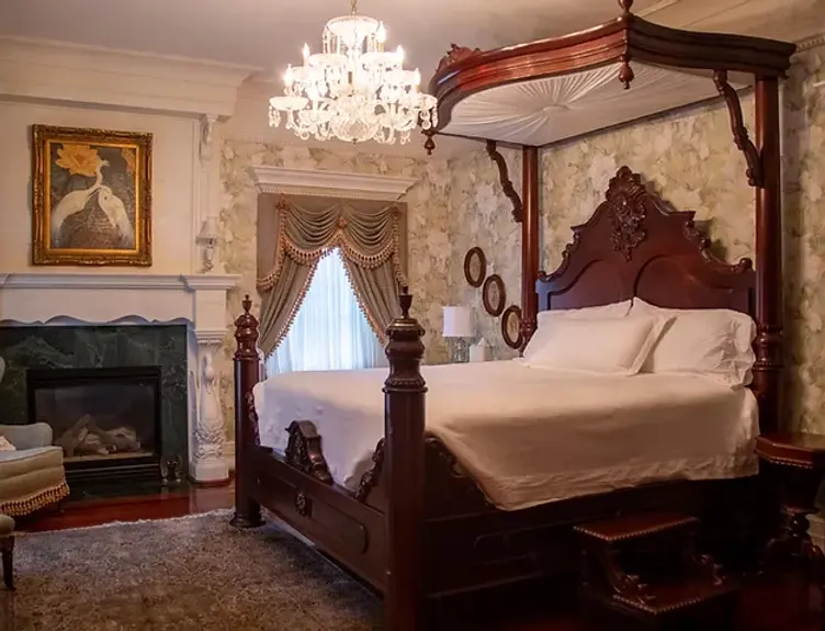 Elegant bedroom with four-poster bed, chandelier, fireplace. Grand Holland Estate provides luxury.