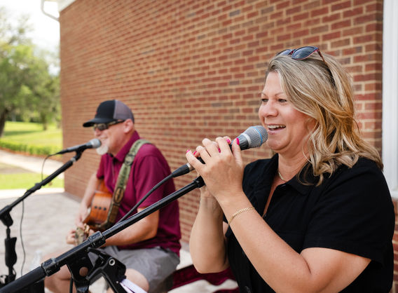 Singing woman with microphone, man playing guitar, brick wall background performance.
