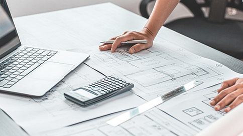 Architect reviewing blueprints with calculator and laptop on desk.