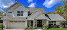 White two-story house with a garage, blue sky, and green yard.