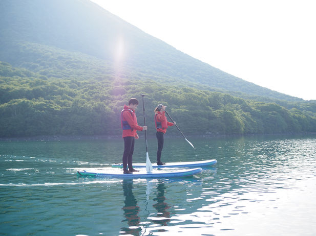 男体山をバックにSUPに立つ男女