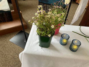 A potted plant with delicate white flowers sitting on a white tableclothed table with two candles in blue votive jars.