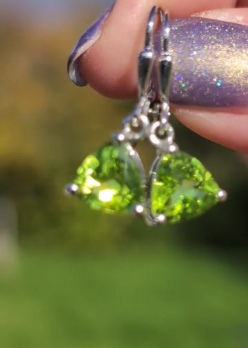 Thumbnail: Silver earrings, with trillion shaped vivid green peridot gemstones dangle from silver hooks
