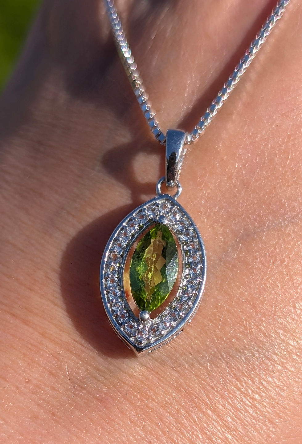 Thumbnail: A silver pendant in a marquise shape set with a vivid green peridot and small white topaz around it