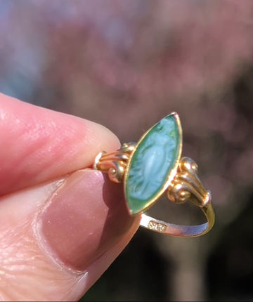 Thumbnail: antique yellow gold ring with ornamental scrolls either side of a nevette shaped green white agate cameo of a roped maiden
