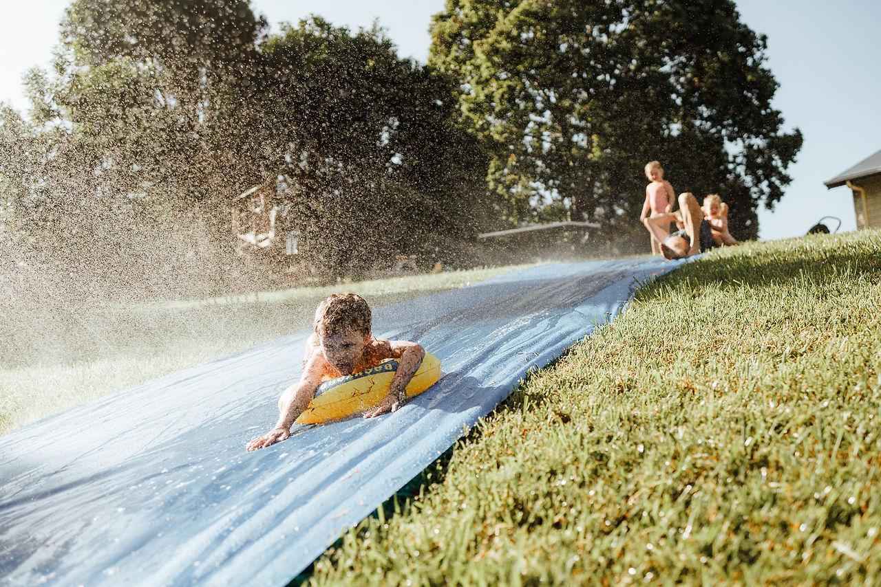 Boy sliding down slip and slide with sprinklers during in home family photography session in Rockhampton  with Sarah Joy, a Rockhampton family photographer
