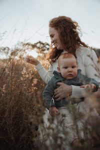 Candid photo of mum and baby in tall grass surrounded by warm light