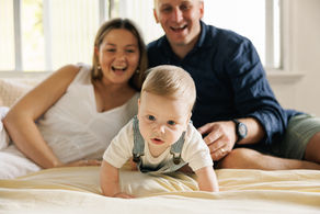 Mum and dad cheering crawling baby on bed during in home session in Rockhampton
