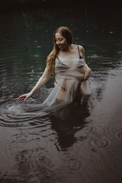 Maternity photo in the water near Yeppon wrapped in tulle with rain drops on the water