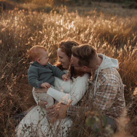  Mum holding her child in a sunlit long grass field during a family photography session in Rockhampton, captured at golden hour.