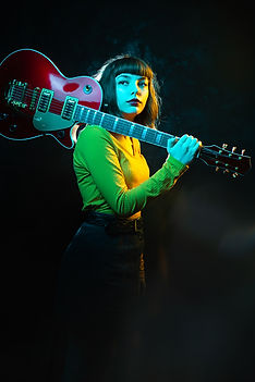 Hipster woman with curly hair with red guitar in neon lights. Rock musician with electrica