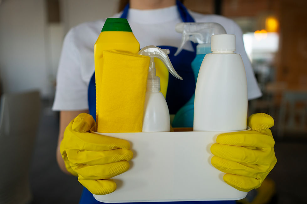 Persoon in blauwe schort en gele handschoenen houdt mand met schoonmaakmiddelen vast. Heldere kleuren, focus op reiniging.