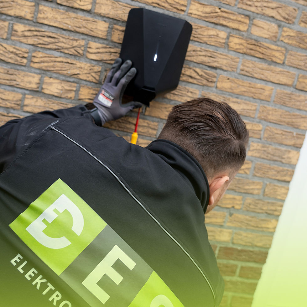 Monteur van DES Elektrotechniek installeert een laadpaal naast een woning, met professioneel gereedschap en beschermende werkkleding.